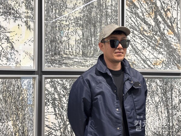 신경철 작가가 리안갤러리 서울에서 열리는 'Light Between Air' 전에 선보인 드로잉 작업 앞에서 포즈를 취했다. 그는 시력문제 때문에 검은 안경을 벗지 못한다.( 사진 함혜리)​